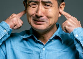 Man in Blue Top Covering Ears With Fingers